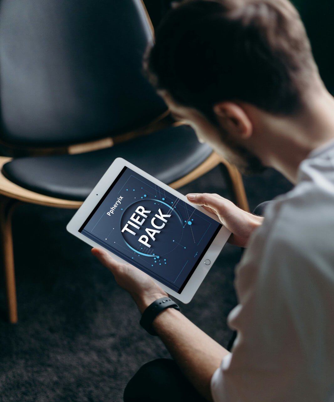 Person holding a tablet with 'TIER PACK' displayed on the screen, sitting in a chair.